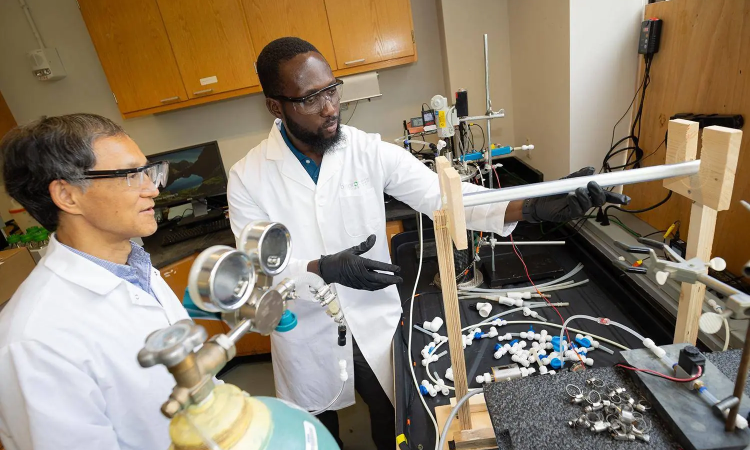 Dr. Yongsheng Chen working with student Ahmed Yunus in a labaratory. Both men are wearing white lab coats and protective glasses