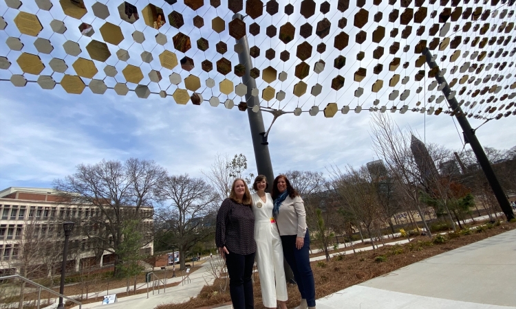 Three women stand beneath a canopy of mirrored hexagon tiles.