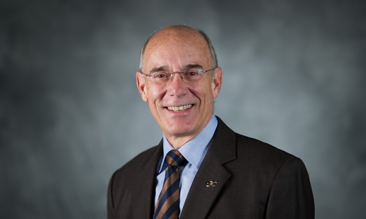 A man wearing a coat and tie smiles in a portrait 