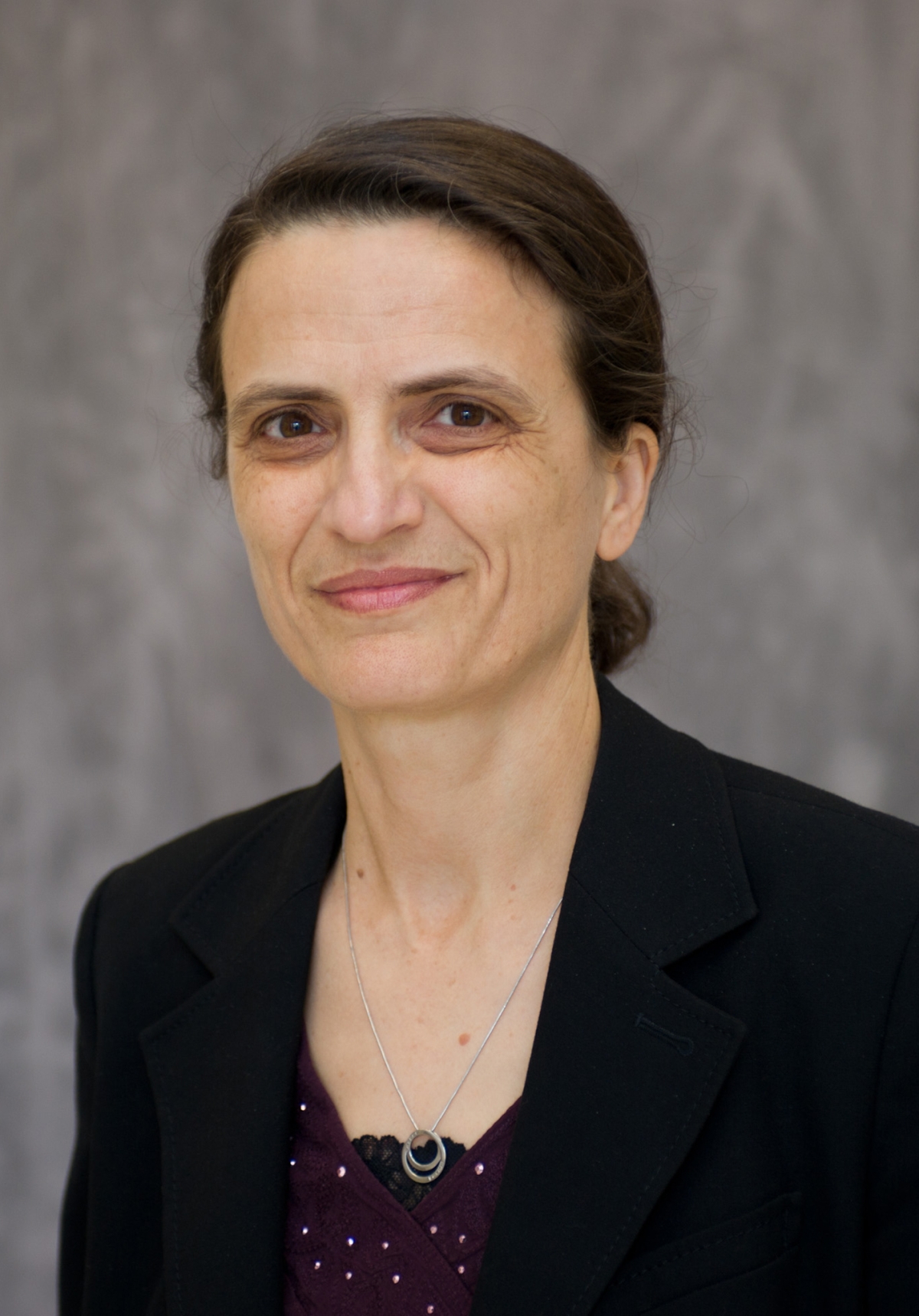 Headshot of a brunette woman in a burgundy patterned top and black blazer jacket