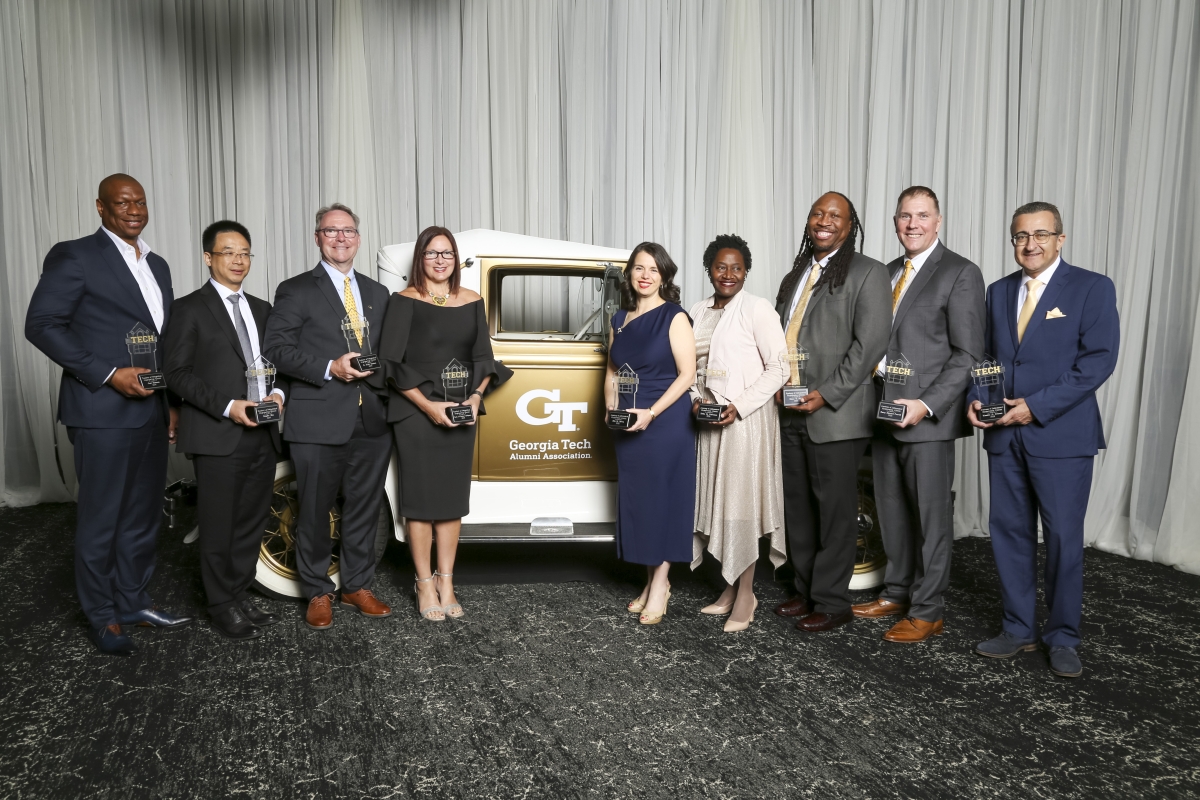 A group of people pose in front of an antique gold car and a white curtain 