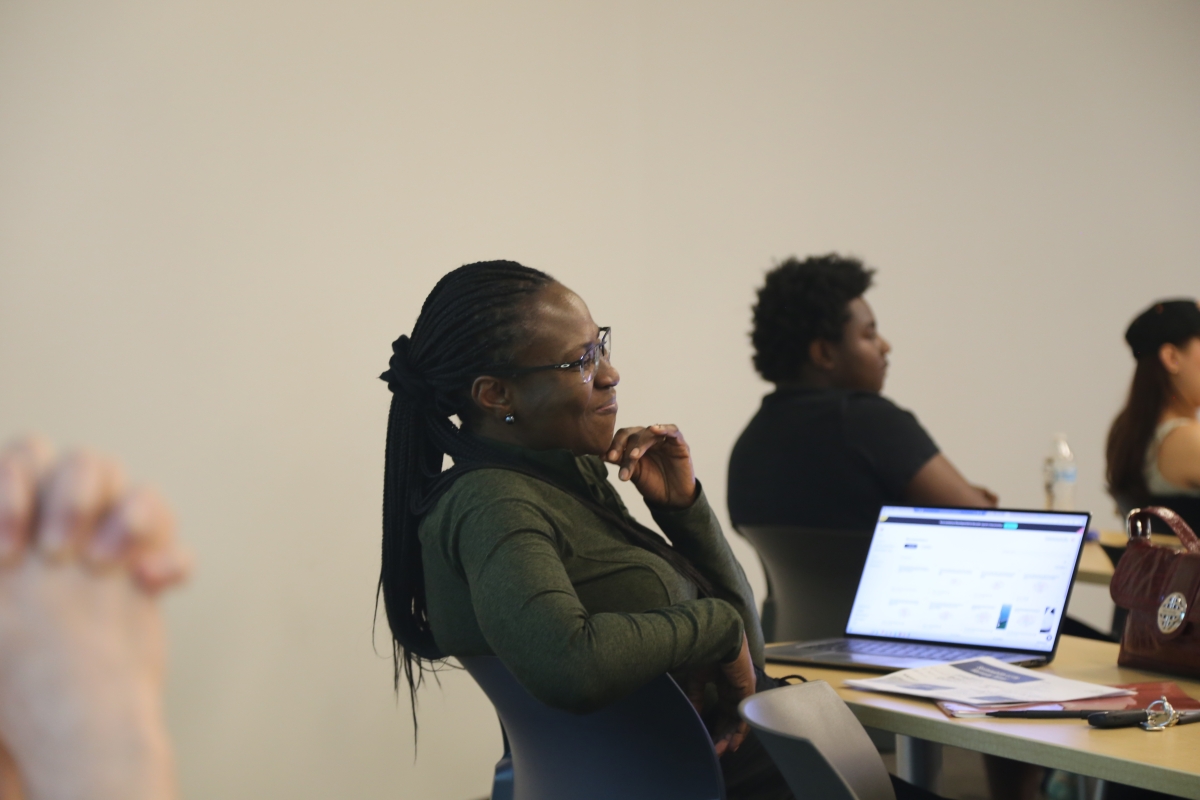 A woman sits in a classroom with a laptop on a desk 