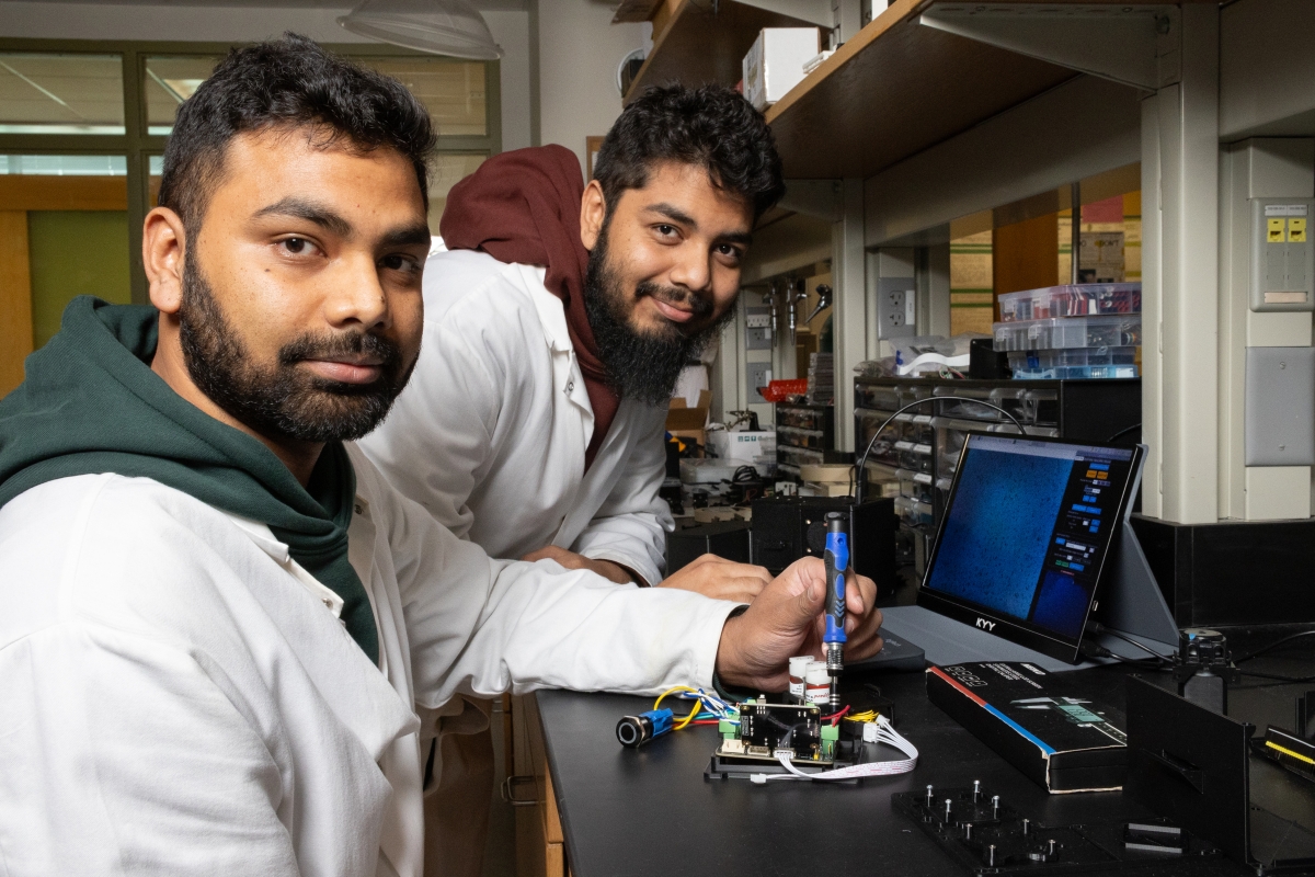two men in lab coats working on an electronic device