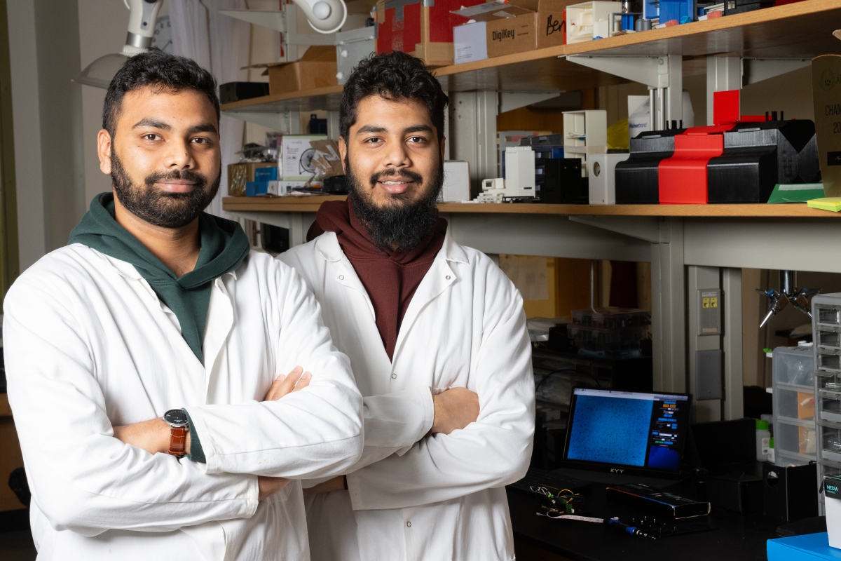 two men pose in white lab coats