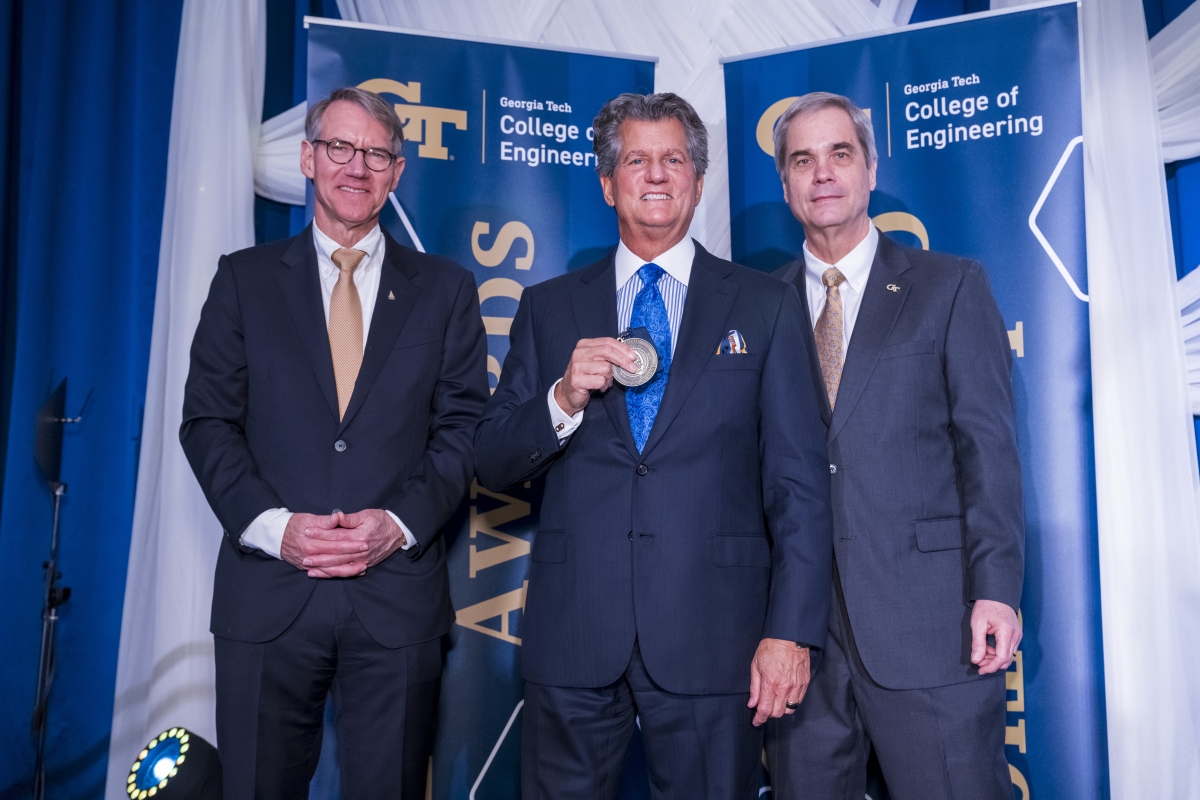 Three men in suits pose with a medal 