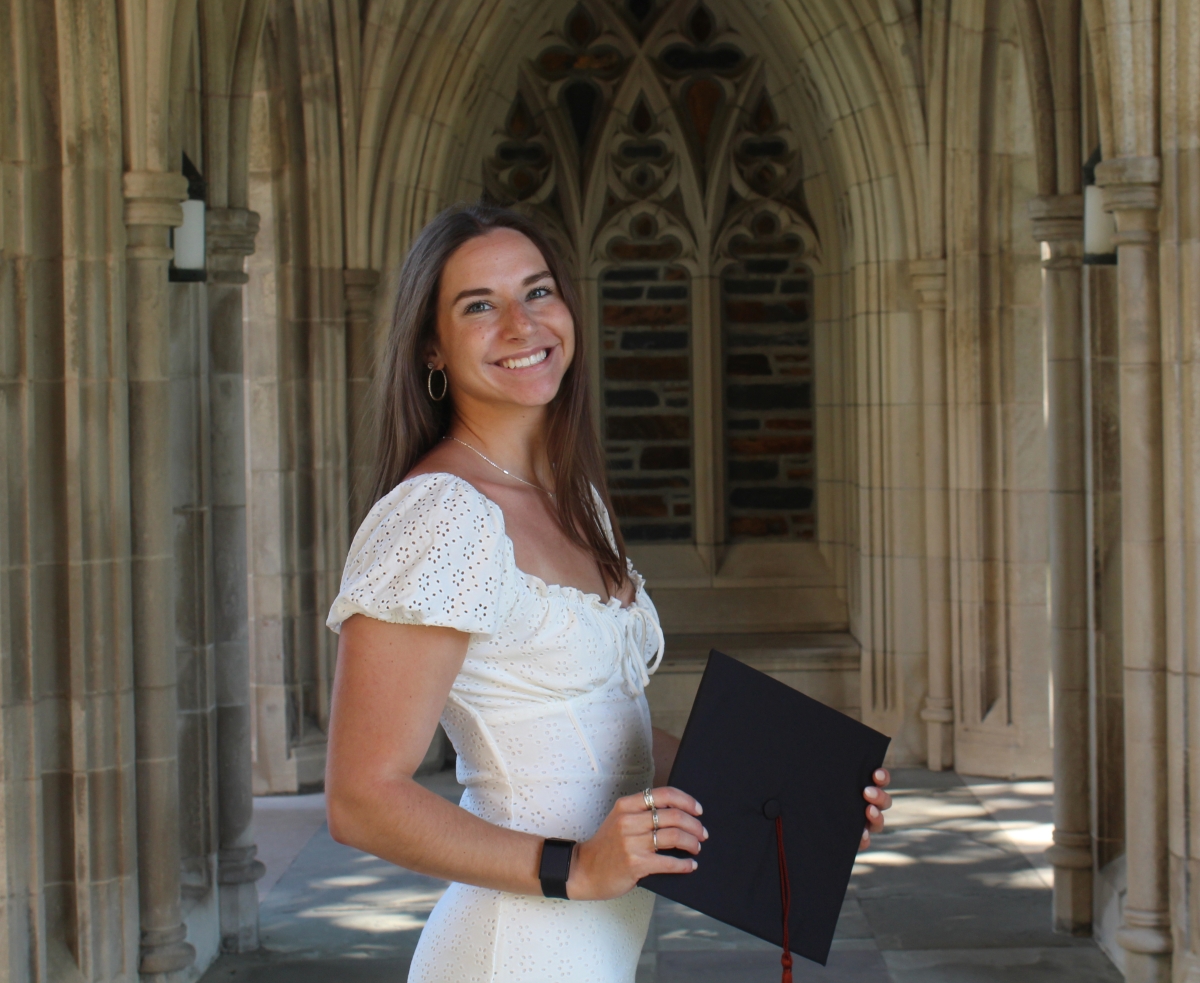 Portrait of Samantha DiLoreto in a white dress holding a graduation mortarboard