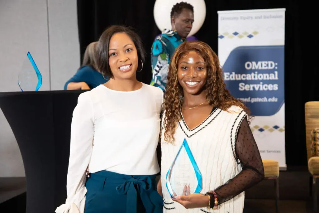 Two women pose for a photo while holding an award