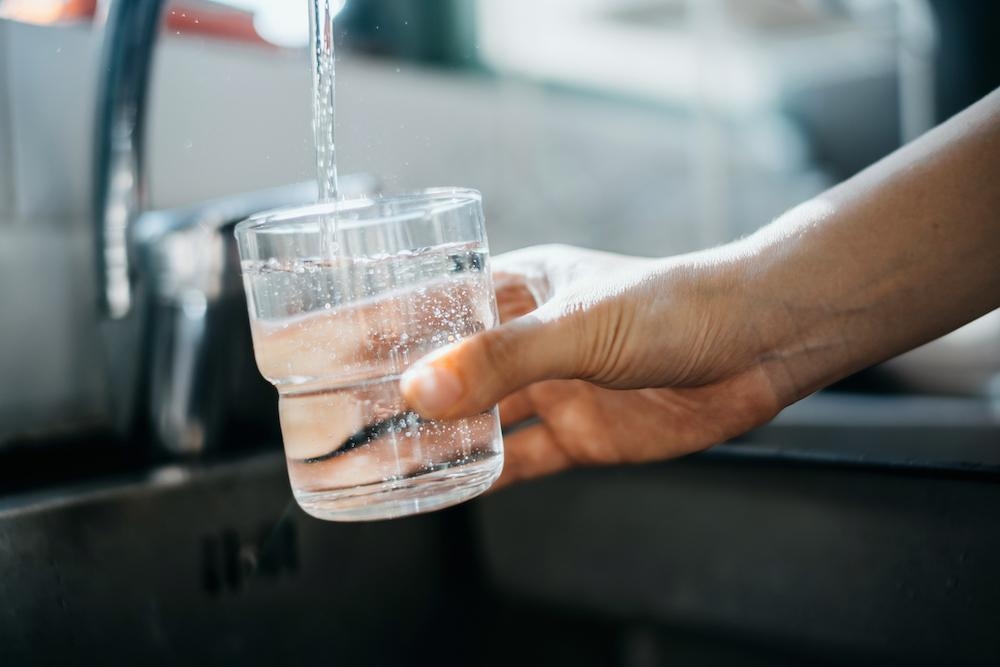 A hand filling a glass with water from a tap