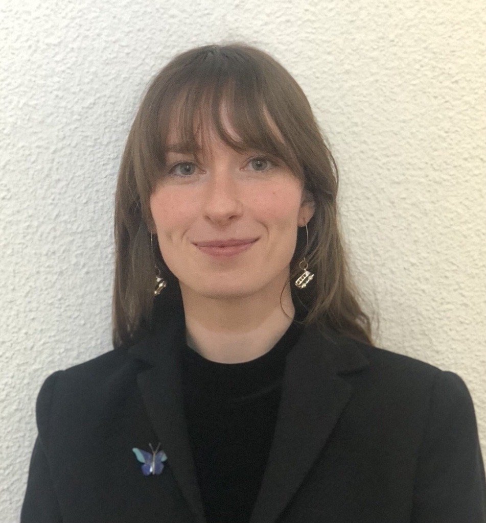 A portrait of Adair Garrett wearing a navy blue blazer with a butterfly pin and a black blouse