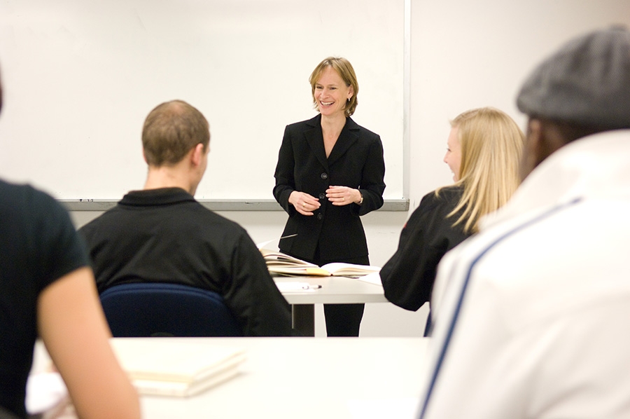 Standing before a white board wearing a black blazer, Lisa Rosenstein leads a class.